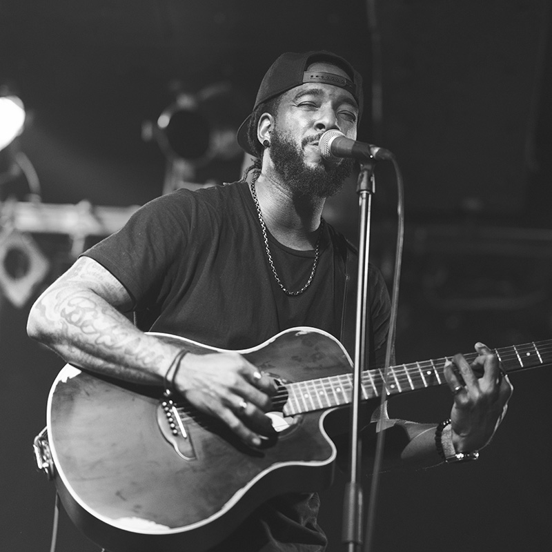 A black man is playing the acoustic guitar and singing passionately on stage